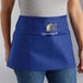 A person wearing a Choice royal blue customizable apron with 3 pockets in a professional kitchen.