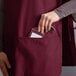 A person putting a card in the pocket of a burgundy cobbler apron.
