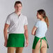 A man and woman standing next to each other wearing Choice Kelly Green standard waist aprons.