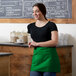 A woman in a green apron standing in front of a counter.