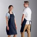 A man and woman wearing navy blue Choice adjustable bib aprons.