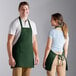 A man and woman wearing Choice hunter green bib aprons standing at a counter in a professional kitchen.