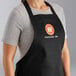 A person wearing a black Choice customizable bib apron with pockets in a professional kitchen.
