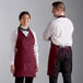 A man and woman wearing burgundy Choice tuxedo aprons.