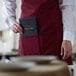 A person wearing a burgundy tuxedo apron with black book in a pocket.