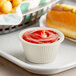 A yellow Carlisle fluted ramekin filled with ketchup on a tray.
