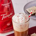 A glass of coffee with Torani Puremade Peppermint Bark Flavoring Sauce, whipped cream, and a red and white striped straw.
