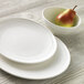 A pear in a Libbey Royal Rideau white porcelain bowl next to a white plate.