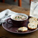 A Libbey matte mulberry porcelain soup mug filled with soup and a slice of bread on a plate.