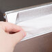 A hand pulling a tissue from a black Vollrath wall-mounted napkin dispenser.