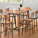 A Lancaster Table & Seating wooden table base with chairs and wine glasses on it.