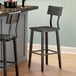 A Lancaster Table & Seating rustic industrial bar height chair with an antique slate gray finish next to a bar.