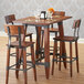A Lancaster Table & Seating wooden bar height table base with chairs and glasses on it.