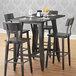 A Lancaster Table & Seating rustic wooden bar height table base with chairs and glasses on it.