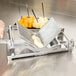 A person using a Vollrath CubeKing Cheese Slicer to cut cheese on a metal tray.
