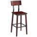 A Lancaster Table & Seating rustic industrial bar height chair with mahogany finish and a black seat on a bar table.