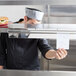 A chef using a Thunder Group Stainless Steel Wall Mounted Ticket Holder to hold a receipt over a counter with food.