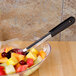 A bowl of fruit salad with a spoon on a counter.