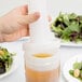 A hand pouring brown salad dressing into a Carlisle white plastic container with a brown lid.