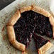 A pie with a slice missing and a piece of dough on a table with a Lucky Leaf Premium Cherry Fruit Filling & Topping pail.