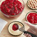 A person using a spoon to spread Lucky Leaf strawberry pie filling in a pie crust.