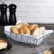 An American Metalcraft Zorro rectangular basket filled with rolls on a table.