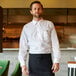 A man wearing a white Henry Segal dress shirt and black pants and apron standing in a restaurant.
