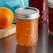 A close-up of a Ball Half-Pint Quilted Crystal Canning Jar filled with orange jam next to an orange.