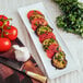 An American Metalcraft curved edge porcelain serving platter with sliced tomatoes and garlic.