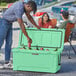 A man wearing a hat putting a can into a CaterGator Seafoam outdoor cooler while a woman and child smile at the camera.