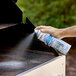 A person using SC Johnson fantastik Max Oven and Grill Cleaner to spray a grill.