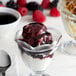 A glass cup with a scoop of ice cream and black raspberry topping.