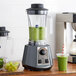 A AvaMix commercial blender filled with a green drink on a counter with a green smoothie and grapes.