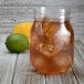 A Fineline plastic mason jar filled with ice and tea with ice and limes, with a lemon and lime next to it.