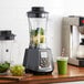 An AvaMix commercial blender filled with green juice, spinach, and fruit on a counter.
