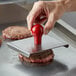 A person using a Prince Castle meat press to stamp a meat patty on a griddle.