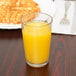 A Cambro clear plastic tumbler filled with orange juice on a table in a breakfast diner.