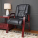 A Boss black leather mid back guest chair with mahogany finish next to a table with a lamp.