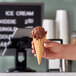 A hand holding a JOY waffle cone with chocolate ice cream.