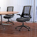 A group of Boss black mesh office chairs and wood tables in a room.