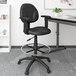 A black Boss drafting stool with adjustable arms and footring next to a desk.
