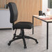 A Boss black fabric multi-function task chair with wheels next to a desk.