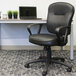 A black Boss LeatherPlus office chair with loop arms in front of a table with a laptop on it.