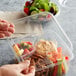 A person holding a Fabri-Kal Greenware clear plastic container filled with salad and fruit.