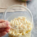 A hand holding a Fabri-Kal clear plastic deli container filled with macaroni and cheese.