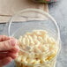 A hand holding a Fabri-Kal clear plastic deli container of macaroni and cheese.