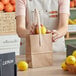 A woman holding a Choice brown paper bag with lemons.
