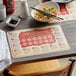 A table set with a white bowl of noodles and chopsticks on a wooden surface with a Chinese Zodiac paper placemat.