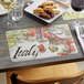 A table set with Italian themed paper placemats, food, and wine glasses.