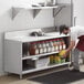 A man putting food on a stainless steel table with an enclosed base and shelf.
